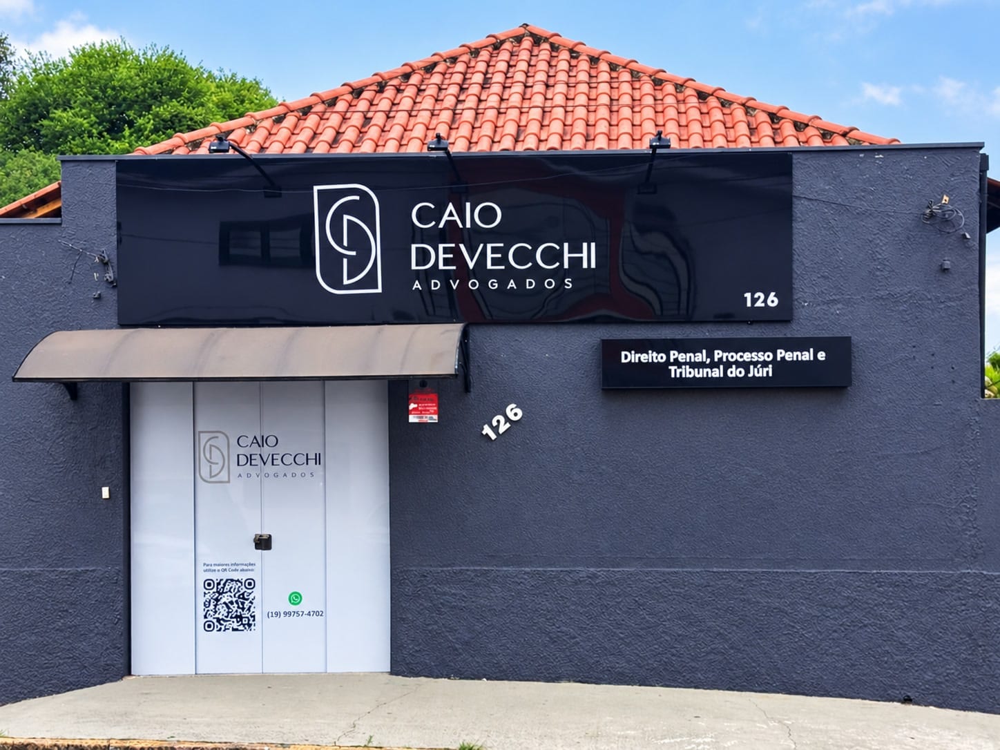 A entrada do escritório na Rua Ademar de Barros, 126: letreiro preto com o monograma e o nome Caio Devecchi Advogados, a porta branca com o QR code e o telefone do WhatsApp, o número 126 na parede e a placa Direito Penal, Processo Penal e Tribunal do Júri.